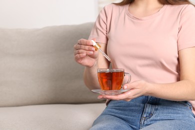 Photo of Woman dripping food supplement into cup of tea indoors, closeup. Space for text