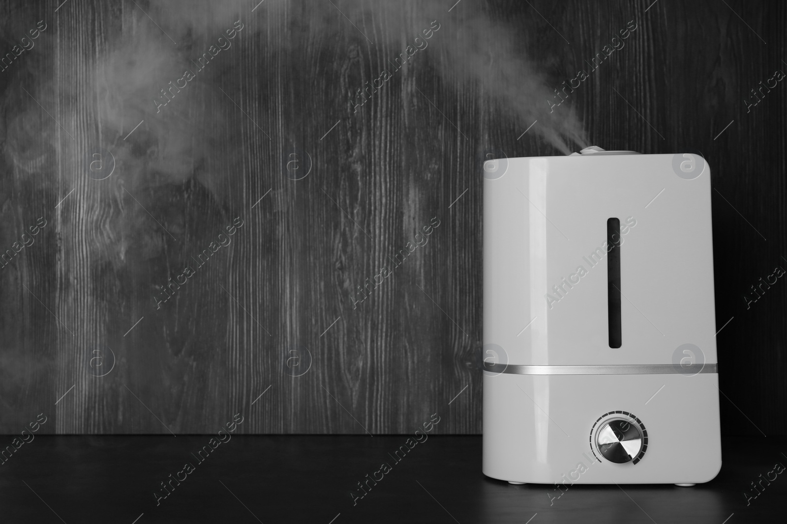 Photo of Modern air humidifier on table against wooden background. Space for text