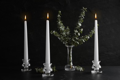 Photo of Elegant candlesticks with burning candles and eucalyptus on black table