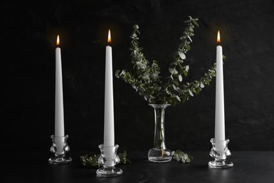 Elegant candlesticks with burning candles and eucalyptus on black table