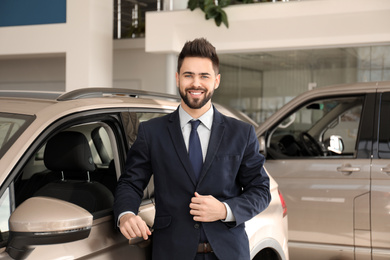 Young salesman near new car in dealership