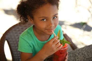 Cute African-American girl with glass of natural lemonade at table in cafe