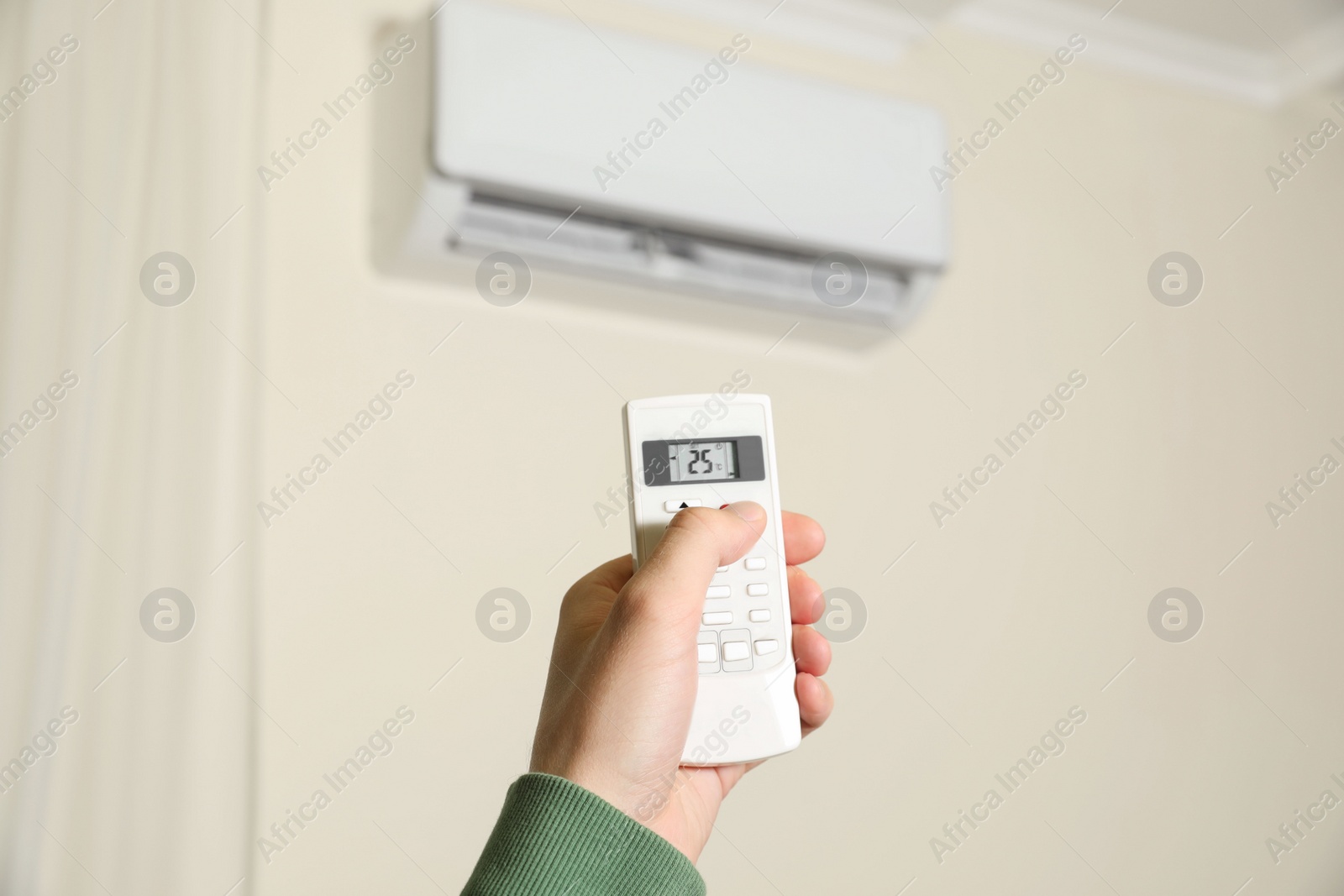 Photo of Man operating air conditioner with remote control indoors, closeup