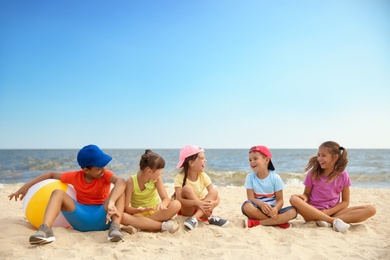 Photo of Group of children sitting on sand at sea beach. Summer camp