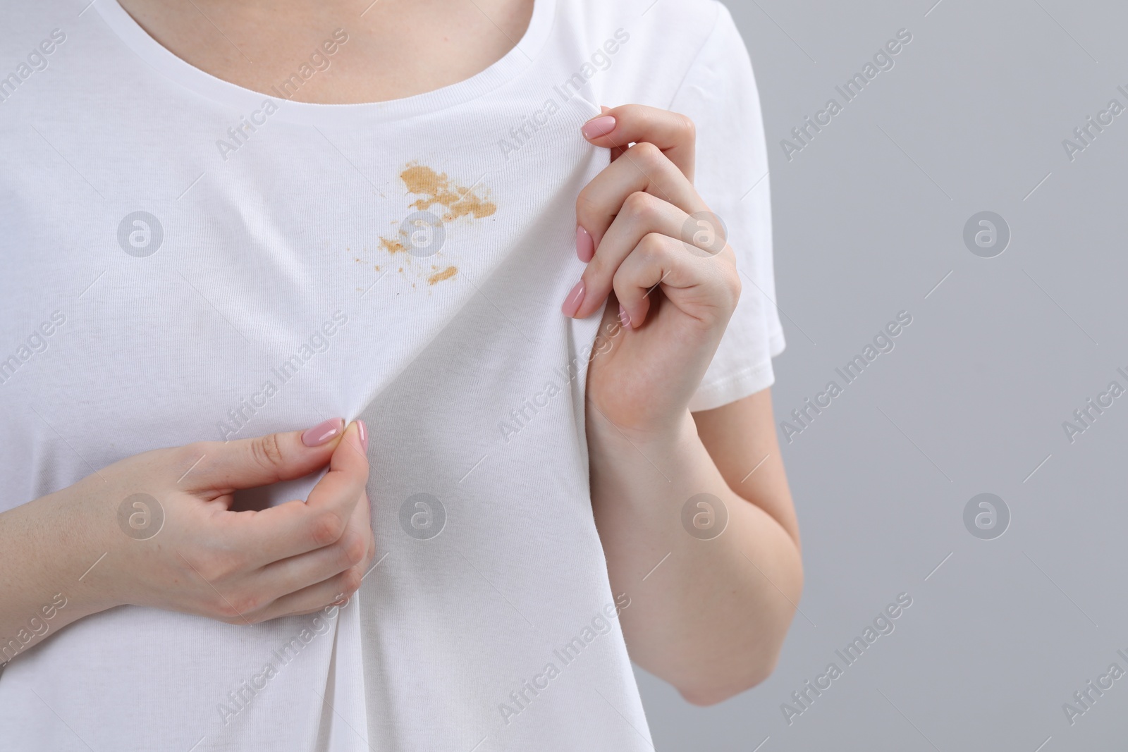 Photo of Woman showing stain on her t-shirt against light grey background, closeup