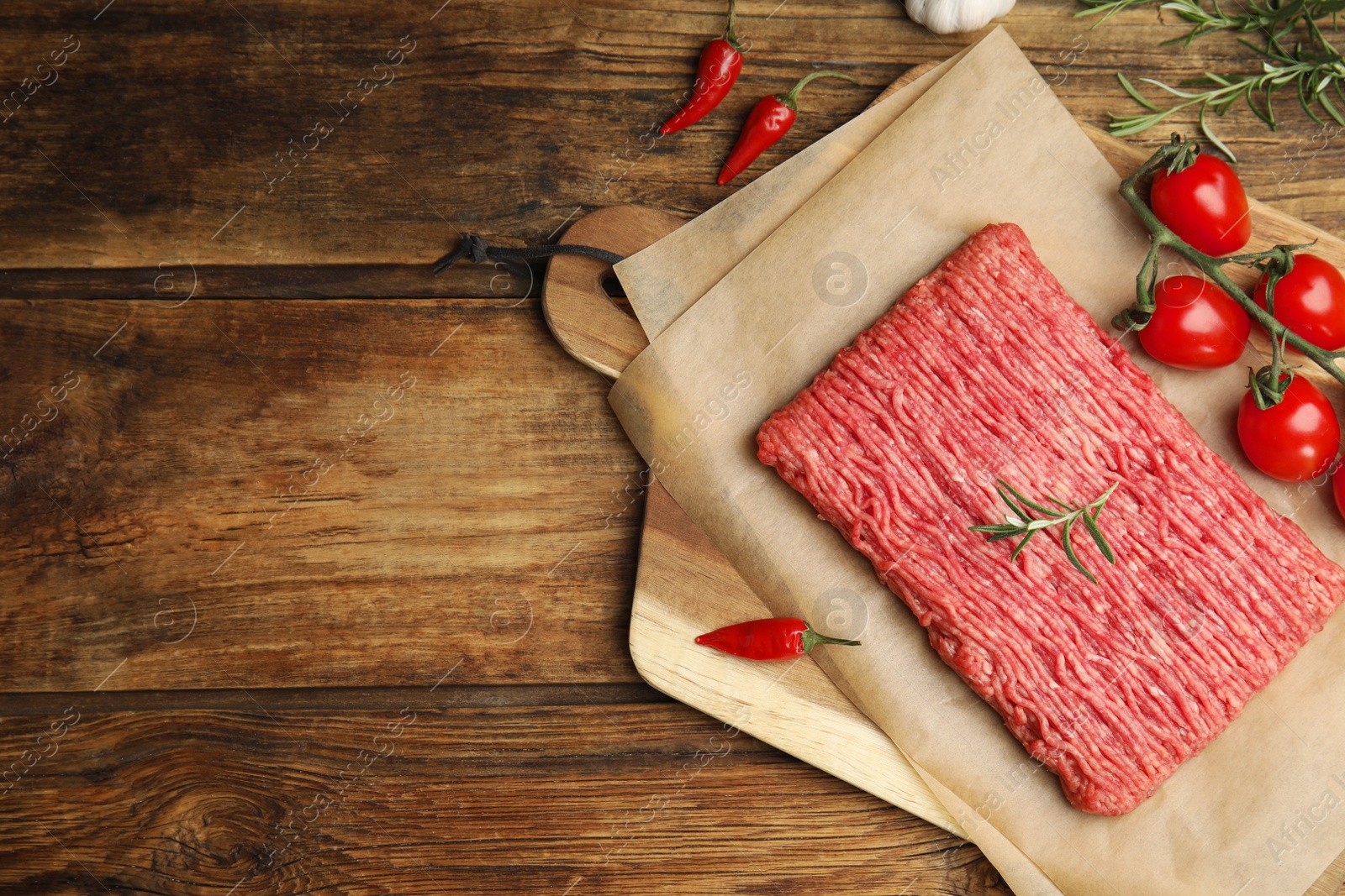 Photo of Raw fresh minced meat, tomatoes and other ingredients on wooden table, flat lay. Space for text