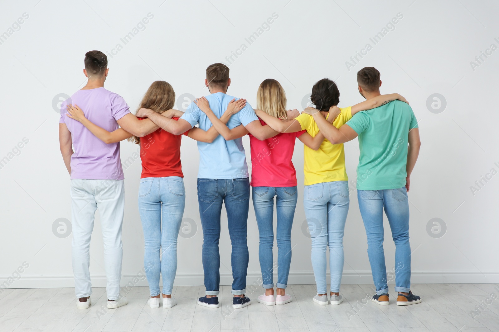 Photo of Group of young people hugging each other near light wall. Unity concept