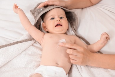 Photo of Woman applying body cream onto baby`s skin on bed, closeup