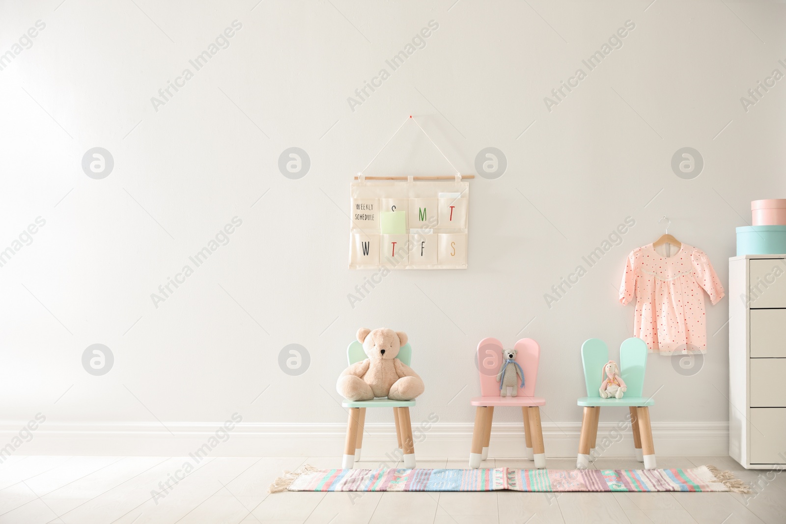 Photo of Cute toys on chairs with bunny ears near white wall indoors, space for text. Children's room interior