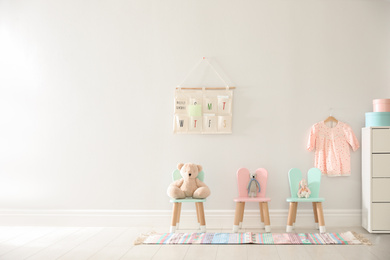 Photo of Cute toys on chairs with bunny ears near white wall indoors, space for text. Children's room interior