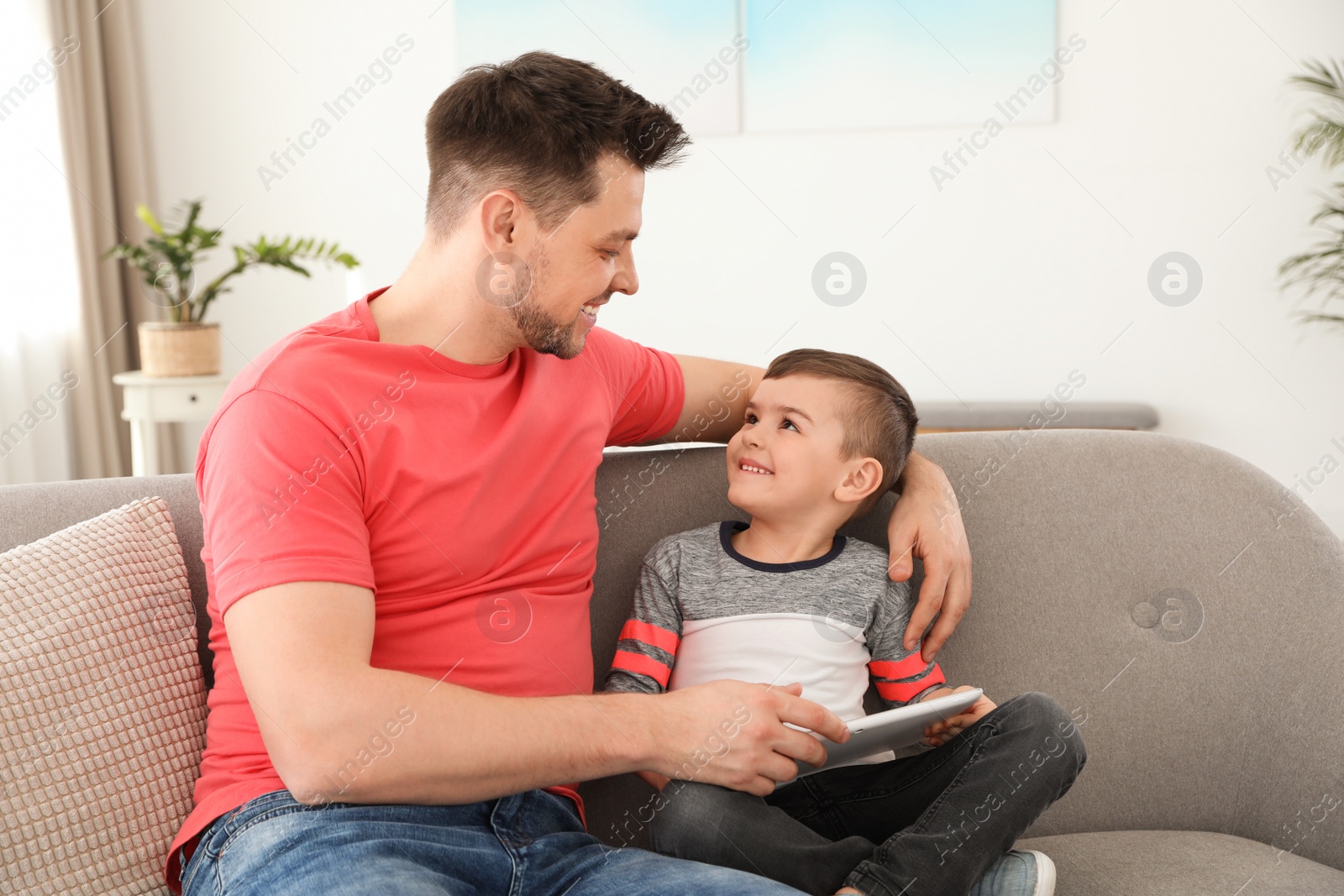 Photo of Boy and his father with tablet sitting on sofa at home. Family time