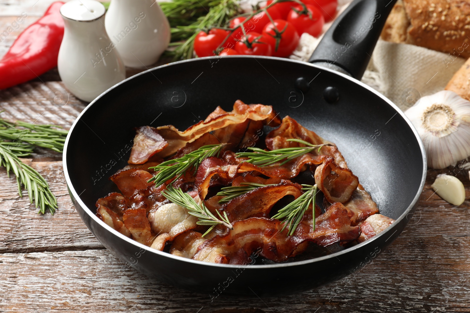 Photo of Delicious bacon slices in frying pan and products on wooden table, closeup