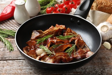 Photo of Delicious bacon slices in frying pan and products on wooden table, closeup