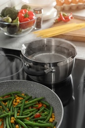 Photo of Pot near frying pan with vegetables on electric stove in kitchen