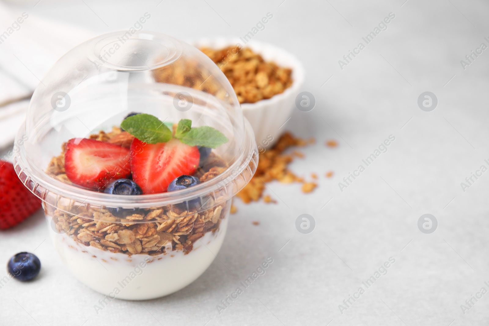 Photo of Tasty granola with berries and yogurt in plastic cup on light table, closeup. Space for text