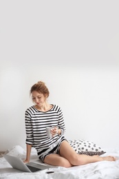 Female blogger with laptop and cup of coffee on bed