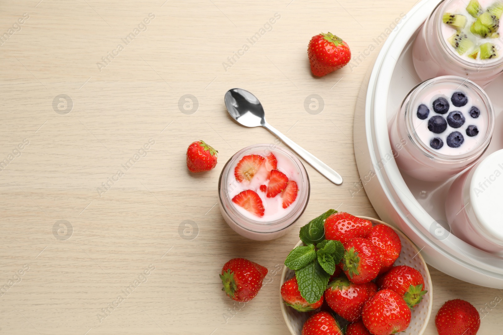 Photo of Yogurt maker with jars and different fruits on wooden table, flat lay. Space for text