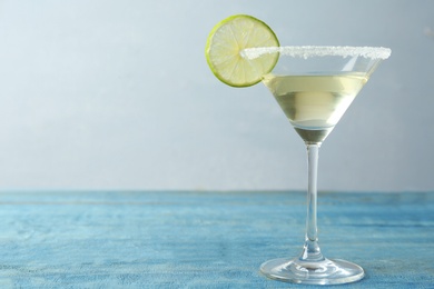 Photo of Glass of Lime Drop Martini cocktail on light blue wooden table. Space for text