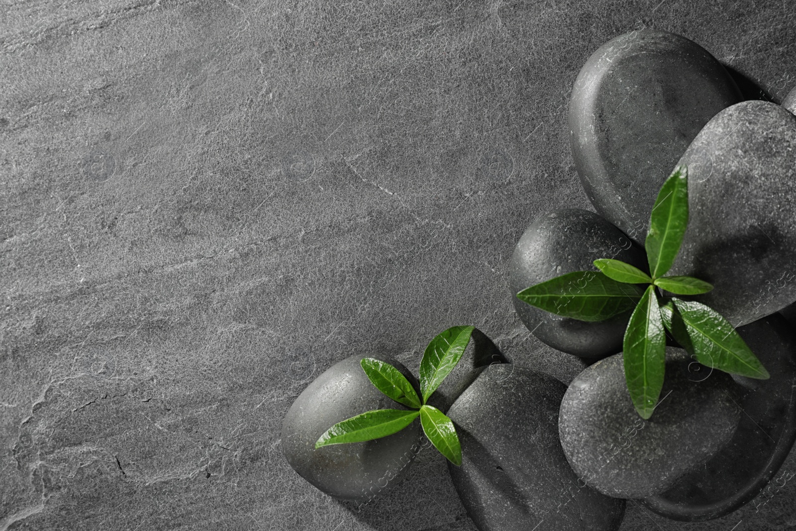 Photo of Spa stones and green leaves on grey table, flat lay with space for text