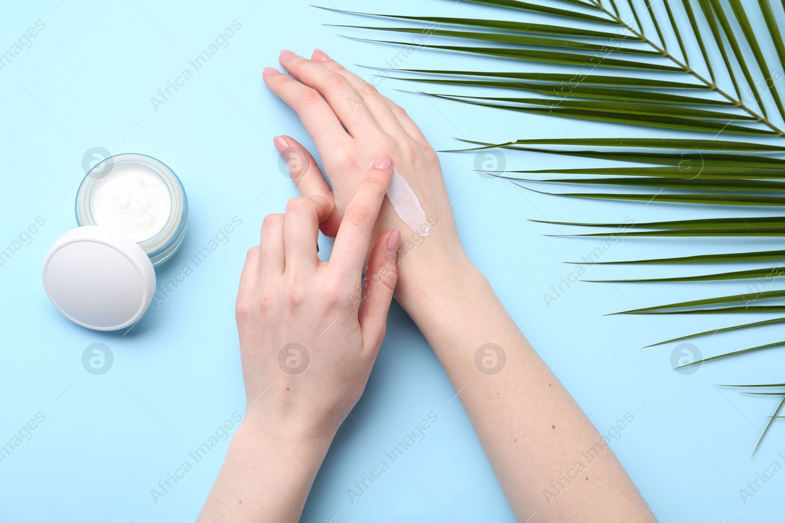 Photo of Woman applying hand cream on light blue background, top view