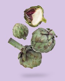 Image of Fresh raw artichokes falling on lavender background