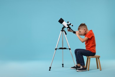 Photo of Little boy looking at stars through telescope on light blue background, space for text