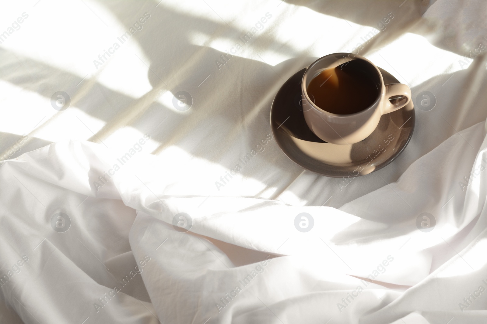 Photo of Cup of aromatic coffee on bed in morning, space for text