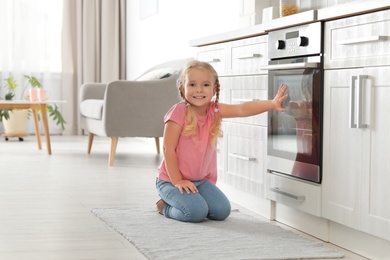 Photo of Little girl sitting near oven in kitchen. Space for text