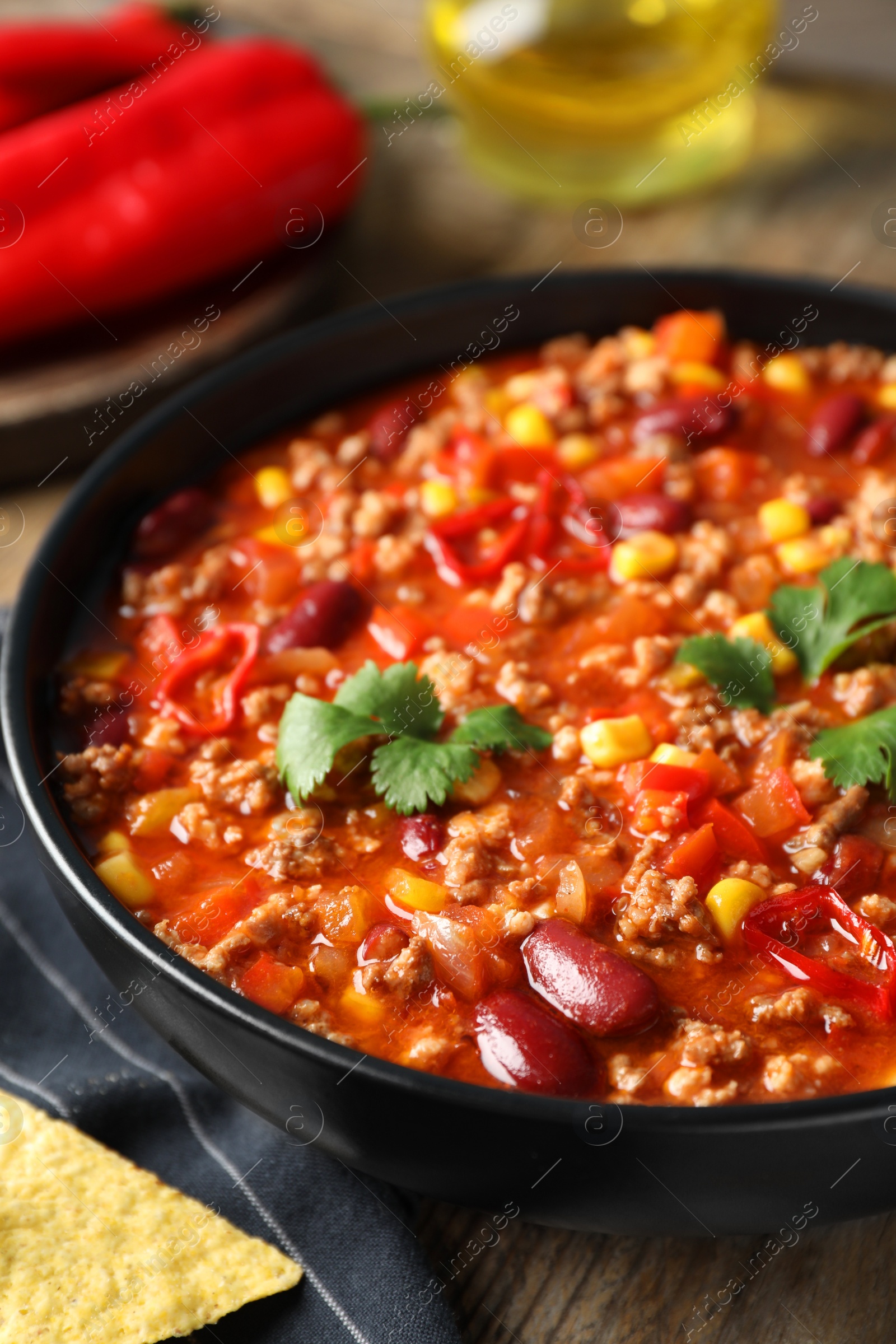 Photo of Bowl with tasty chili con carne on wooden table, closeup