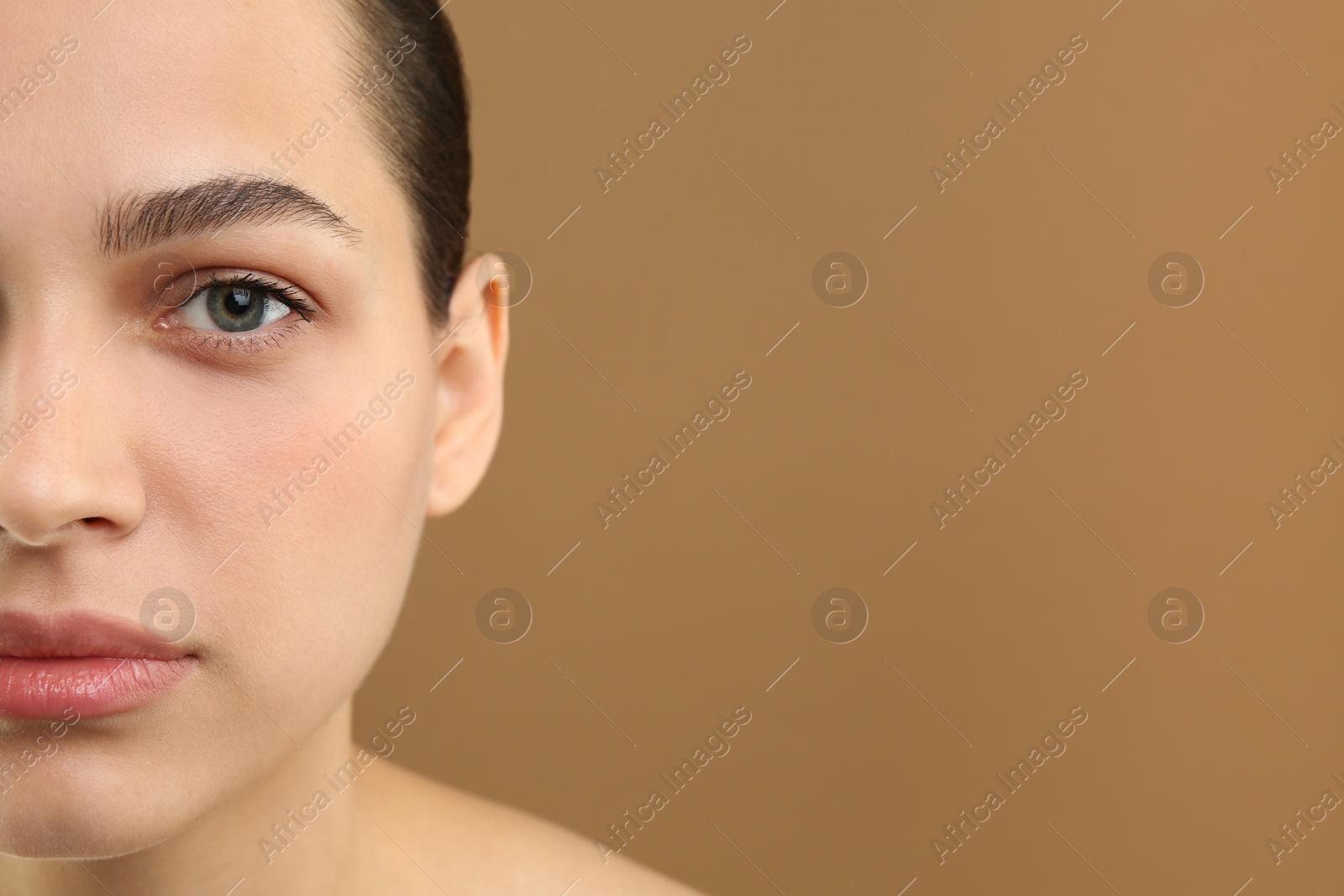 Photo of Young woman with perfect eyebrows on brown background, closeup. Space for text