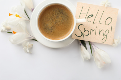 Photo of Card with words HELLO SPRING, cup of coffee and fresh flowers on white background, flat lay