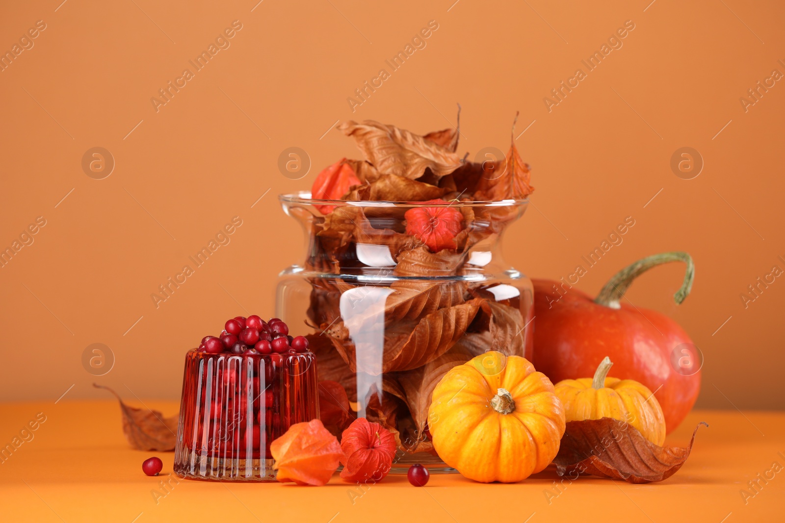 Photo of Composition with beautiful autumn leaves, berries and pumpkins on table against orange background