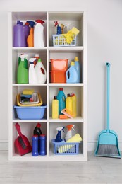 Photo of Shelving unit with detergents and cleaning tools near white wall indoors