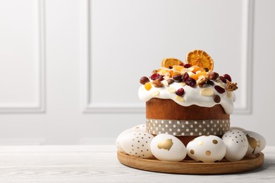 Photo of Traditional Easter cake with dried fruits and decorated eggs on white wooden table indoors. Space for text