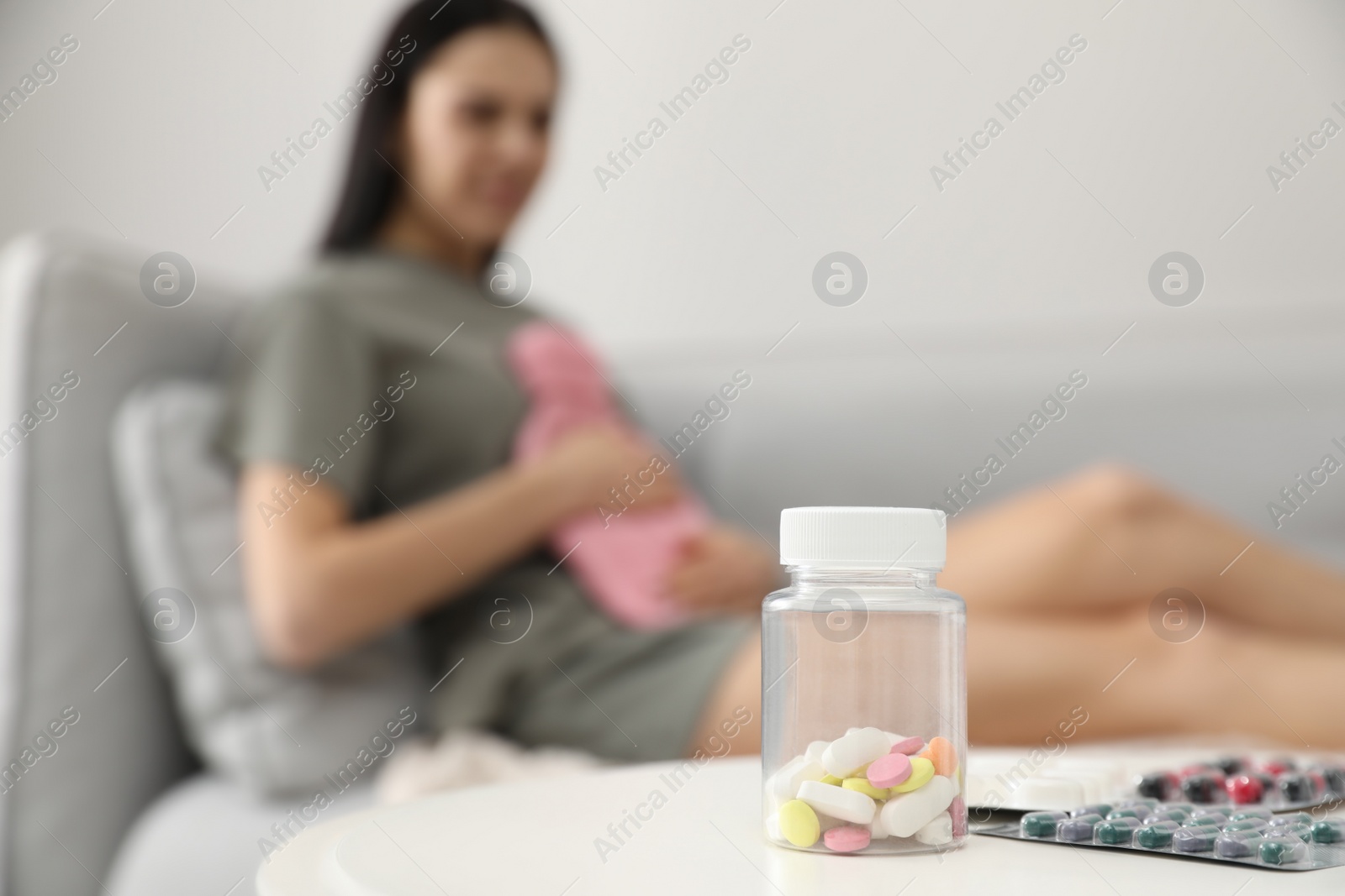 Photo of Woman using hot water bottle to relieve pain at home, focus on pills