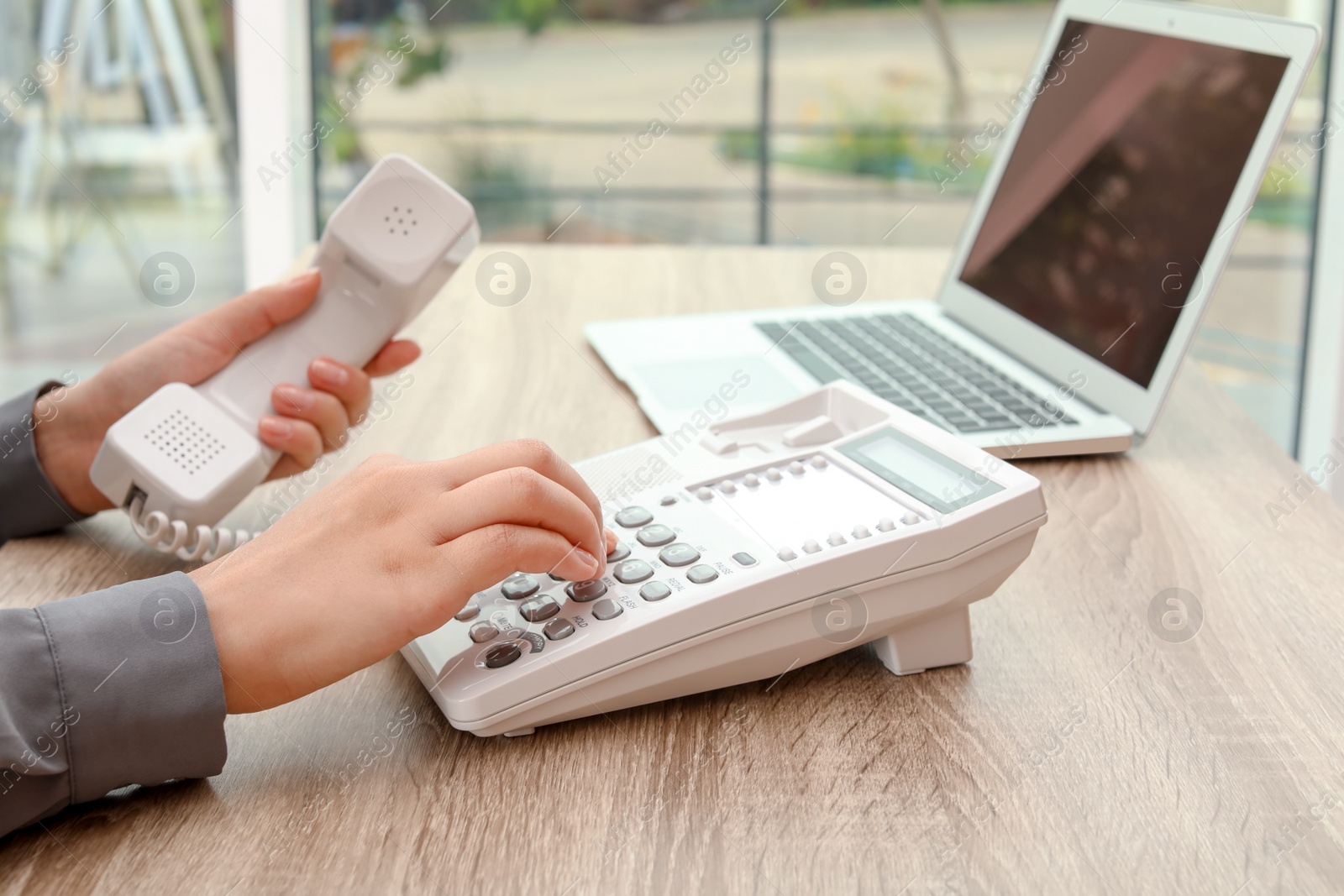 Photo of Woman dialing number on telephone at table indoors, closeup