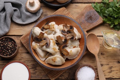 Photo of Delicious dumplings (varenyky) with potatoes, onion and mushrooms served on wooden table, flat lay