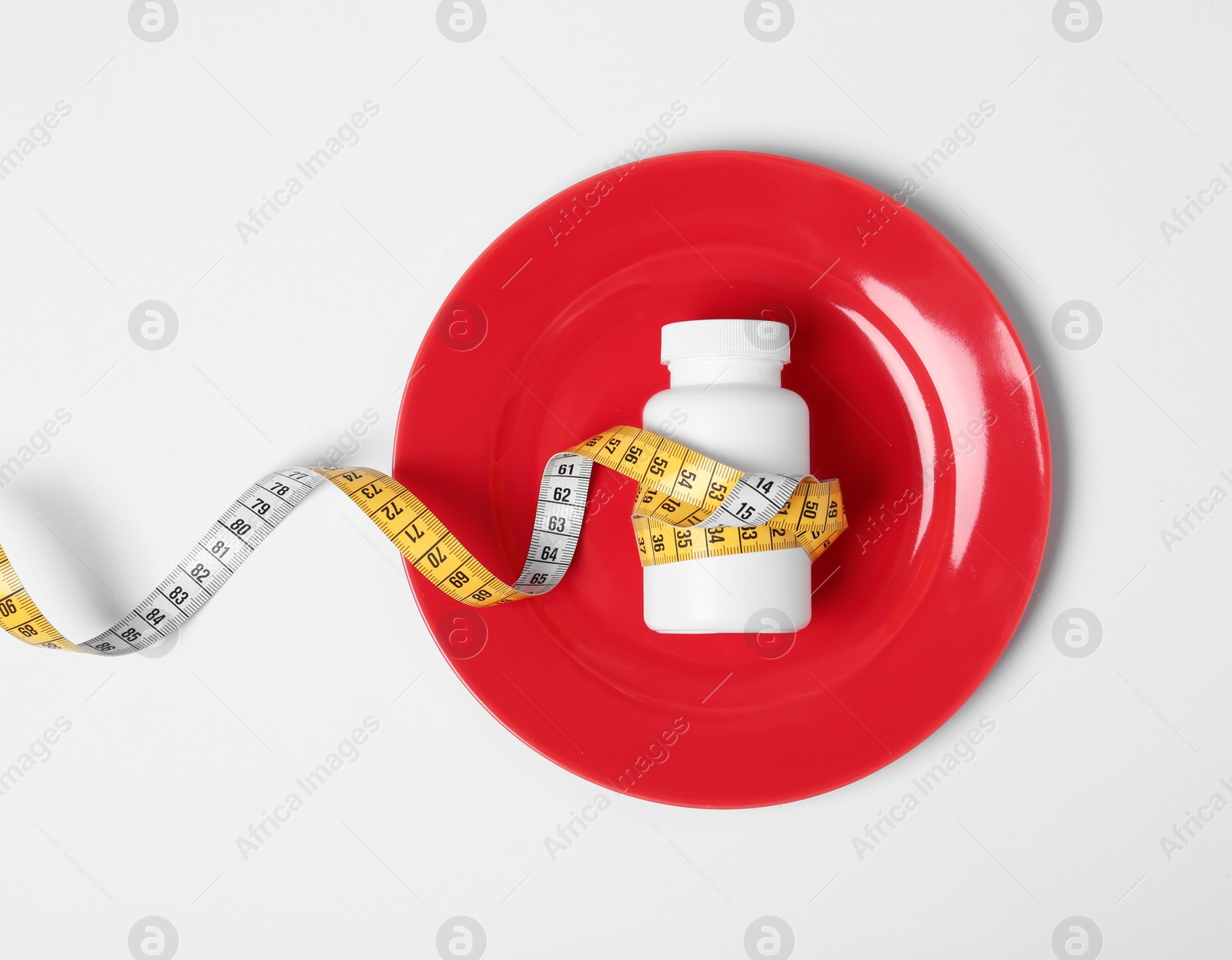 Photo of Plate with bottle of weight loss pills and measuring tape on white background, top view