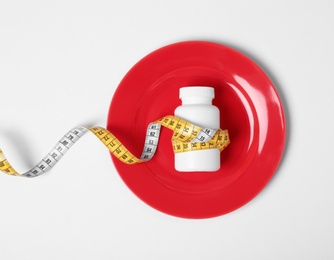 Photo of Plate with bottle of weight loss pills and measuring tape on white background, top view