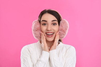 Beautiful young woman wearing earmuffs on pink background