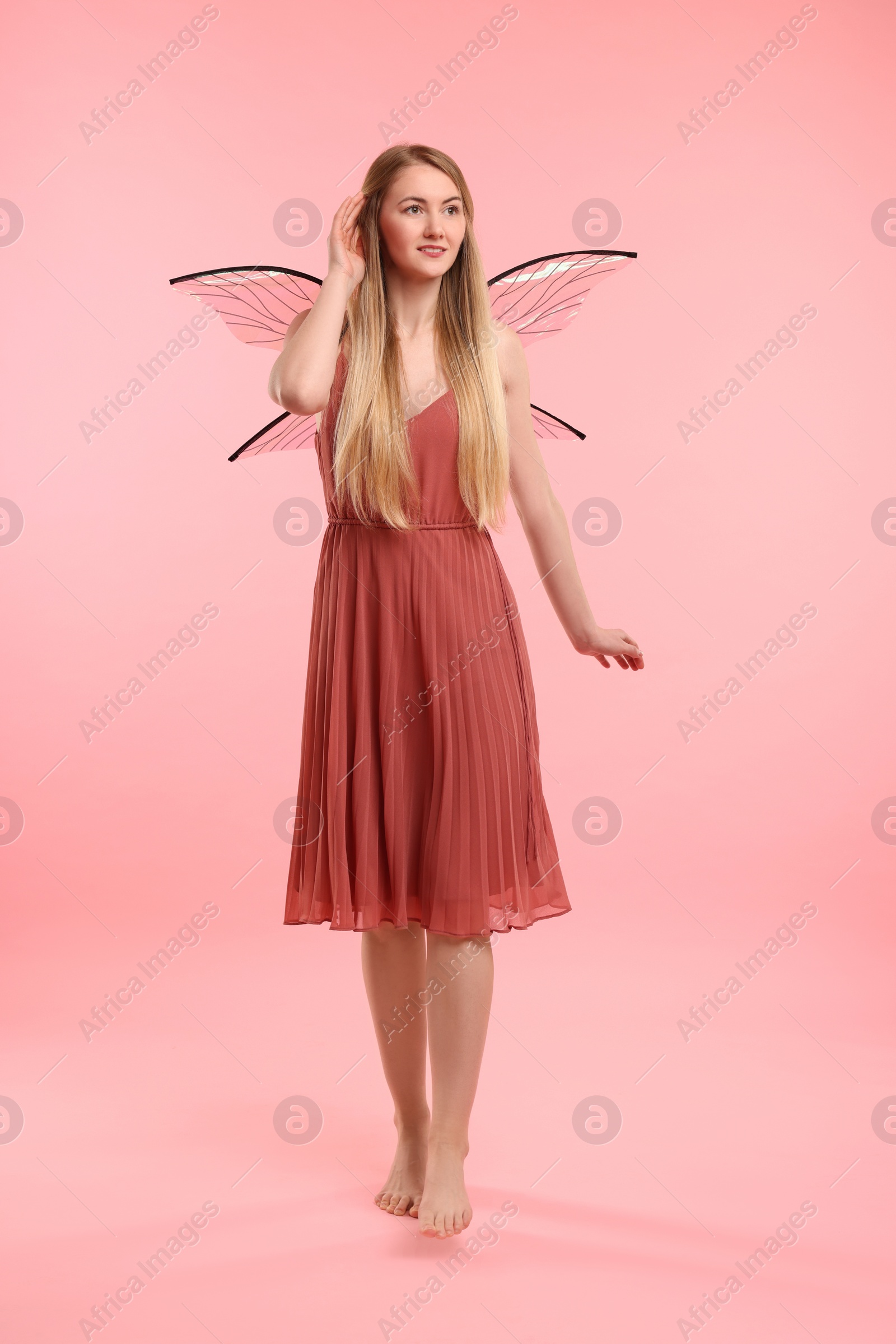 Photo of Beautiful girl in fairy costume with wings on pink background