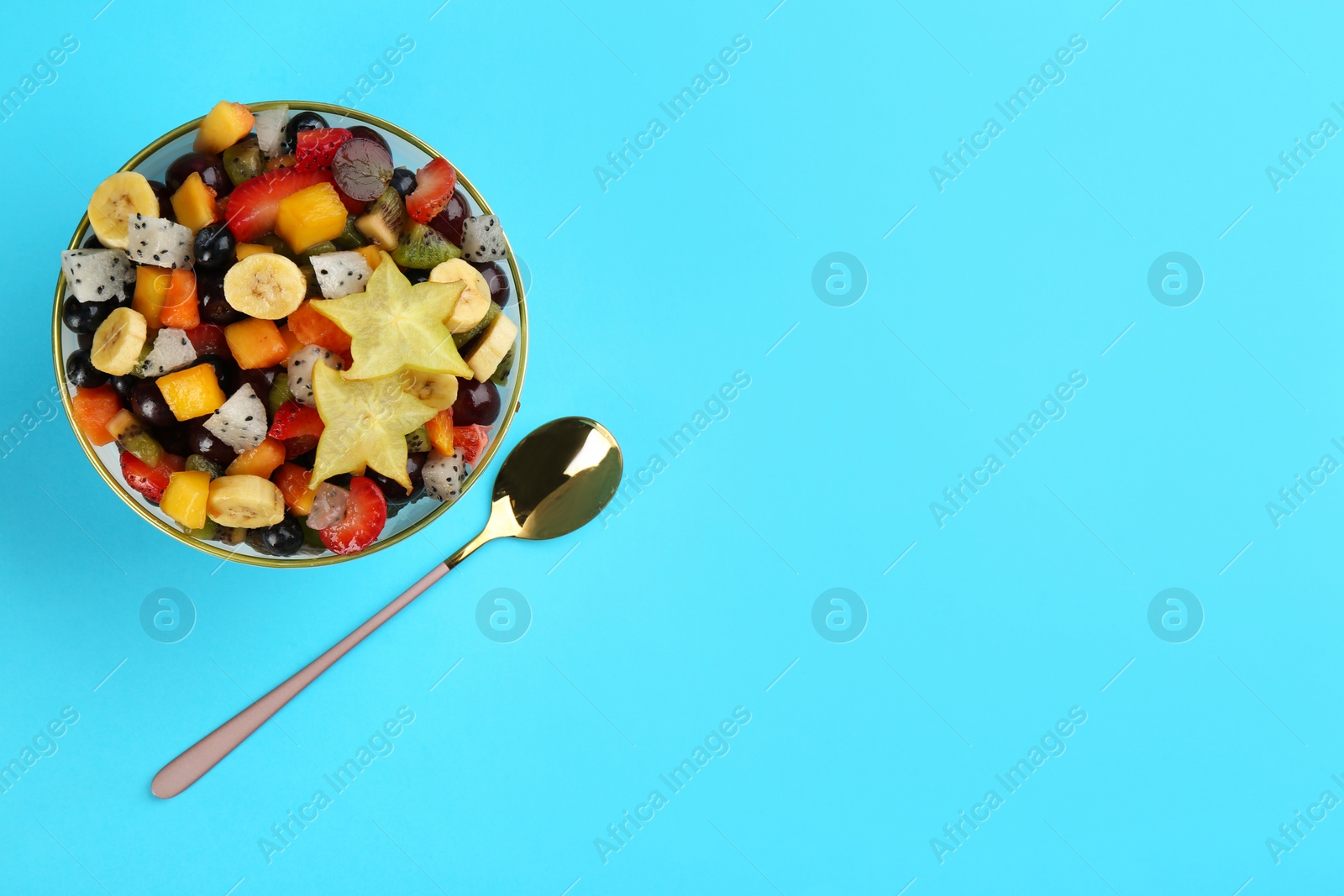 Photo of Delicious exotic fruit salad and spoon on light blue background, flat lay. Space for text