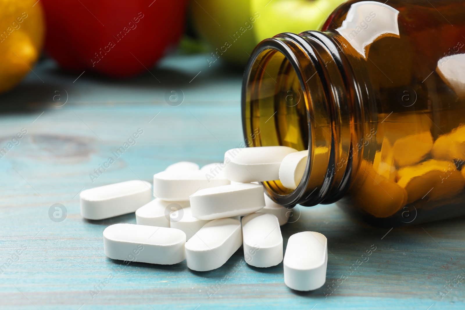 Photo of Dietary supplements. Overturned bottle with pills on light blue wooden table, closeup