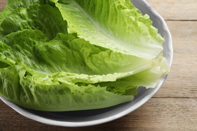 Photo of Bowl with fresh leaves of green romaine lettuce on wooden table, closeup