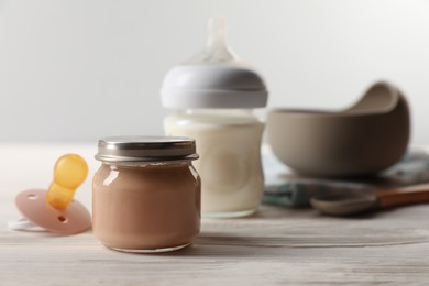 Photo of Jar with healthy baby food and pacifier on white wooden table. Space for text