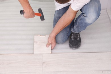 Photo of Man using hammer during installation of new laminate flooring, closeup