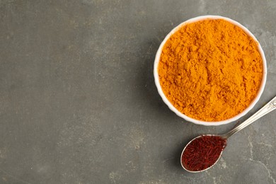 Photo of Bowl of saffron powder and spoon with dried flower stigmas on grey table, flat lay. Space for text