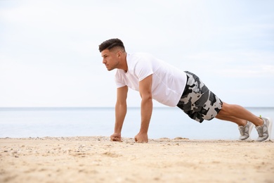 Photo of Muscular man doing push up on beach. Body training