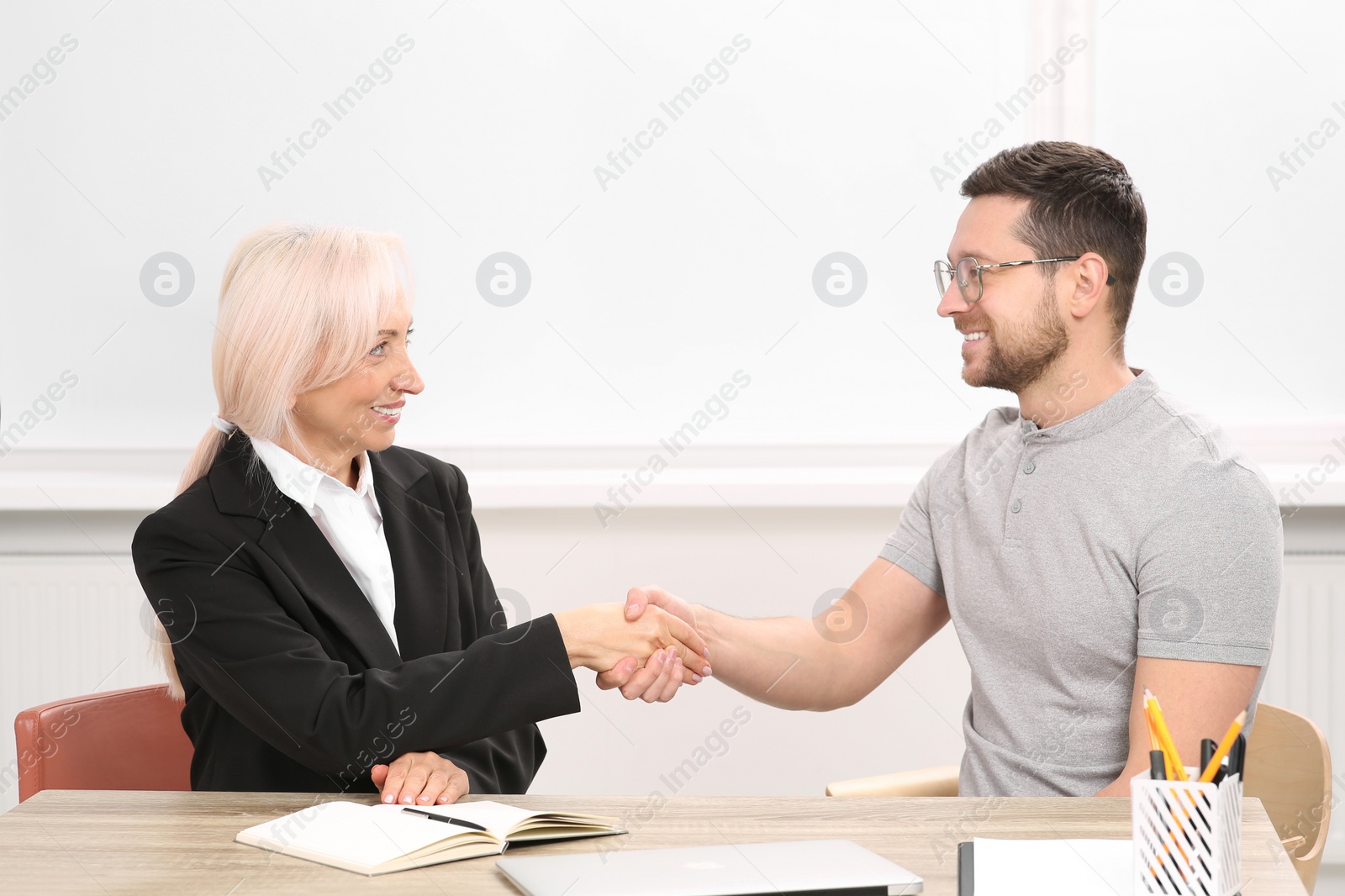 Photo of Happy woman shaking hands with man at wooden table in office. Manager conducting job interview with applicant