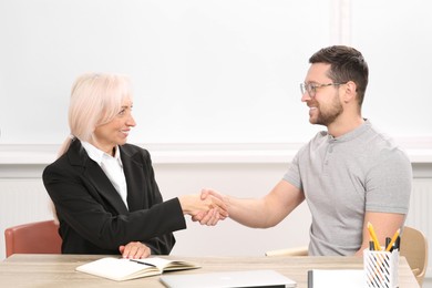 Photo of Happy woman shaking hands with man at wooden table in office. Manager conducting job interview with applicant